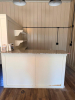 CUSTOM BUILT L SHAPED SERVICE COUNTER WITH POLISHED GRANITE COUNTERTOP, RAISED FRONT AND SIDE PANELS, LOWER GRANITE SERVICE LEDGE, AND THREE WALL-MOUNTED DISPLAY SHELVES WITH DECORATIVE BRACKETS. WHITE PAINTED WOOD CONSTRUCTION WITH LIGHT-COLORED SPECKLED