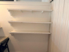 CUSTOM BUILT L SHAPED SERVICE COUNTER WITH POLISHED GRANITE COUNTERTOP, RAISED FRONT AND SIDE PANELS, LOWER GRANITE SERVICE LEDGE, AND THREE WALL-MOUNTED DISPLAY SHELVES WITH DECORATIVE BRACKETS. WHITE PAINTED WOOD CONSTRUCTION WITH LIGHT-COLORED SPECKLED - 4