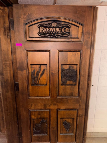 72" WIDE X 80"SOLID WOOD PANEL DOUBLE DOOR WITH DARK STAINED FINISH AND DECORATIVE ROUTED/RAISED PANELS. FEATURES CUSTOM &ldquo;BREWING CO. & DISTILLING&rdquo; GRAPHIC, WHEAT/BARLEY, TRACTOR, BUILDING, AND STATE-SHAPED DECORATIVE DESIGNS INSET INTO THE DOOR. HEAVY-DU