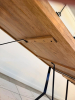 55" X 32" SOLID WOOD DINING / COMMUNITY TABLE WITH WIDE PLANK TOP AND BLACK METAL TRESTLE-STYLE LEGS. NATURAL WOOD TOP FEATURES VISIBLE GRAIN, KNOTS, COLOR VARIATION, AND A LIGHTLY DISTRESSED/RUSTIC FINISH. - 5