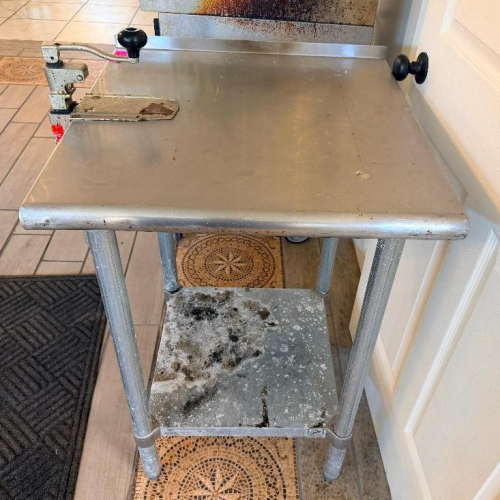 24" W X 24" STAINLESS STEEL WORK TABLE WITH GALVANIZED TUBULAR LEGS, LOWER UNDERSHELF, REAR AND SIDE EDGE GUARDS, AND ATTACHED MANUAL HEAVY-DUTY CAN OPENER WITH ADJUSTABLE VERTICAL POST AND OPERATING HANDLE