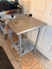 24" W X 24" STAINLESS STEEL WORK TABLE WITH GALVANIZED TUBULAR LEGS, LOWER UNDERSHELF, REAR AND SIDE EDGE GUARDS, AND ATTACHED MANUAL HEAVY-DUTY CAN OPENER WITH ADJUSTABLE VERTICAL POST AND OPERATING HANDLE - 3