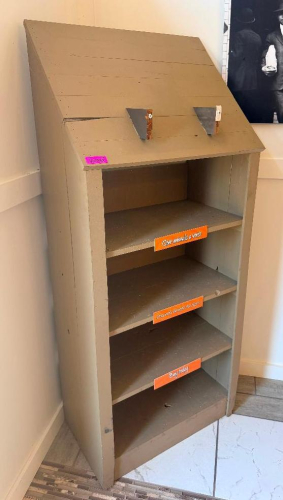 FREESTANDING WOOD DISPLAY SHELVING UNIT WITH SLOPED UPPER SIGN/DISPLAY PANEL, THREE OPEN SHELVES, LOWER BASE SHELF, AND TWO METAL BRACKETS MOUNTED TO THE UPPER PANEL. PAINTED GRAY FINISH