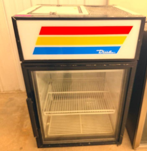 TRUE COUNTERTOP GLASS DOOR MERCHANDISER REFRIGERATOR WITH BLACK CABINET, SINGLE HINGED GLASS DOOR, INTERIOR WIRE SHELVING, AND ILLUMINATED TOP SIGN PANEL.