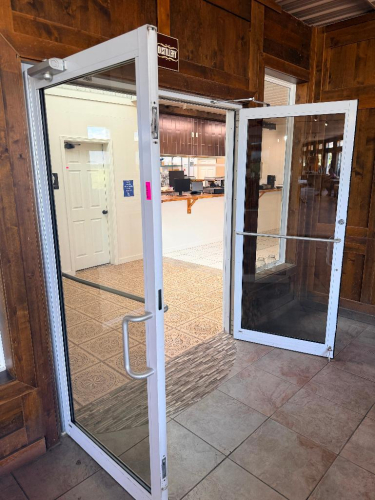 PAIR OF COMMERCIAL FULL-VIEW ALUMINUM-FRAMED GLASS ENTRY DOORS WITH CLEAR TEMPERED GLASS PANELS, PULL HANDLES, HORIZONTAL PUSH BARS, OVERHEAD HYDRAULIC DOOR CLOSERS, HINGE HARDWARE, AND ASSOCIATED FRAME COMPONENTS. WHITE FINISH.