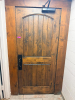 SOLID CORE WOOD DOOR WITH STAINED FINISH, ARCHED RAISED PANEL DESIGN, HEAVY-DUTY HINGES, METAL PULL HANDLE, AND OVERHEAD HYDRAULIC DOOR CLOSER.