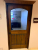 SOLID CORE WOOD DOOR WITH STAINED FINISH, LARGE ARCHED GLASS UPPER PANEL, LOWER VERTICAL PLANK-STYLE RAISED PANEL, WOOD TRIM, AND ROUND DOOR KNOB.