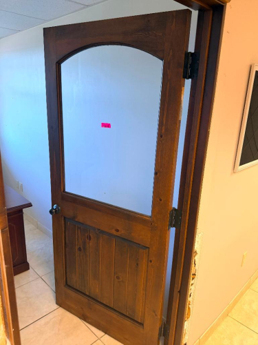 SOLID CORE WOOD DOOR WITH STAINED FINISH, LARGE ARCHED GLASS UPPER PANEL, LOWER VERTICAL PLANK-STYLE RAISED PANEL, WOOD TRIM, AND ROUND DOOR KNOB.