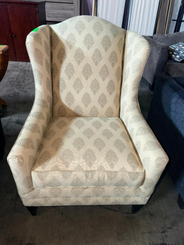 UPHOLSTERED WINGBACK ACCENT CHAIR WITH HIGH BACK, CURVED WING SIDES, PADDED ARMS, REMOVABLE SEAT CUSHION, CREAM / BEIGE FABRIC WITH REPEATING GRAY MEDALLION PATTERN, AND DARK FINISHED WOOD LEGS.