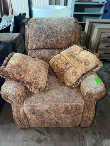 UPHOLSTERED OVERSIZED RECLINER CHAIR WITH BROWN AND TAN PAISLEY PATTERN FABRIC, PADDED ROLLED ARMS, CUSHIONED BACKREST, AND MATCHING DECORATIVE THROW PILLOWS.