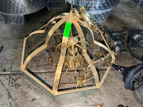 BRASS AND GLASS HANGING CHANDELIER FEATURING A GEOMETRIC METAL FRAME WITH CLEAR GLASS PANELS, MULTIPLE CANDELABRA-STYLE LIGHT SOCKETS, DECORATIVE CENTER COLUMN, HANGING CHAIN, AND CEILING CANOPY. BRASS-TONE FINISH.