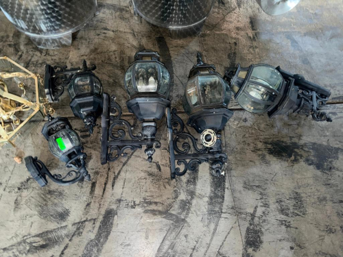 (5) DECORATIVE EXTERIOR WALL-MOUNT LANTERN LIGHT FIXTURES WITH BLACK METAL HOUSINGS, CLEAR GLASS PANELS, ORNATE SCROLL-WORK MOUNTING ARMS, AND DECORATIVE FINIALS. ASSORTED SIZES AND DESIGNS.
