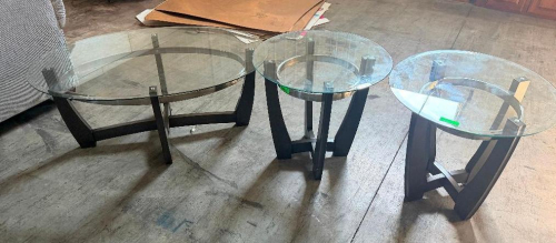 THREE-PIECE GLASS-TOP TABLE SET CONSISTING OF ONE OVAL COFFEE TABLE AND TWO ROUND END TABLES. FEATURES CLEAR GLASS TOPS WITH DARK FINISH WOOD/WOOD-COMPOSITE BASES AND CIRCULAR SUPPORT ACCENTS.