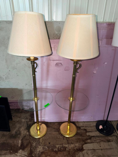 (2) MATCHING BRASS-TONE FLOOR LAMPS WITH INTEGRATED ROUND GLASS TRAY TABLES, ROUND METAL BASES, DECORATIVE ACCENTS, AND CREAM FABRIC LAMP SHADES.