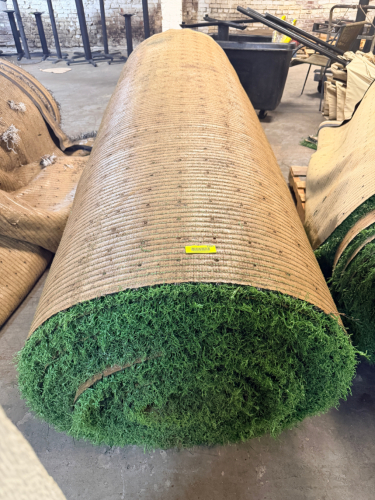 7.5' W X 40' L ARTIFICIAL TURF / ASTROTURF WITH GREEN SYNTHETIC GRASS SURFACE AND WOVEN BACKING. TURF IS ROLLED FOR STORAGE AND SHOWS VISIBLE DIRT, WEAR, FRAYING, AND RESIDUE CONSISTENT WITH PREVIOUS INSTALLATION AND REMOVAL.