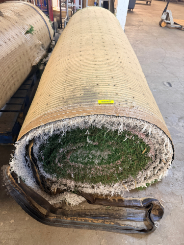 7.5' W X 40' L ARTIFICIAL TURF / ASTROTURF WITH GREEN SYNTHETIC GRASS SURFACE AND WOVEN BACKING. TURF IS ROLLED FOR STORAGE AND SHOWS VISIBLE DIRT, WEAR, FRAYING, AND RESIDUE CONSISTENT WITH PREVIOUS INSTALLATION AND REMOVAL.