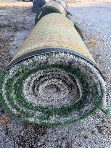 7.5' W X 40' L ARTIFICIAL TURF / ASTROTURF WITH GREEN SYNTHETIC GRASS SURFACE AND WOVEN BACKING. TURF IS ROLLED FOR STORAGE AND SHOWS VISIBLE DIRT, WEAR, FRAYING, AND RESIDUE CONSISTENT WITH PREVIOUS INSTALLATION AND REMOVAL.