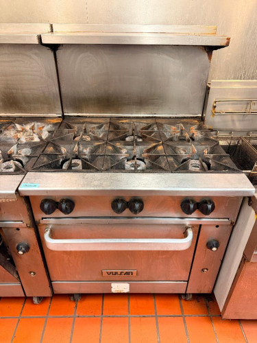 VULCAN COMMERCIAL SIX-BURNER NATURAL GAS RANGE WITH STANDARD OVEN BASE, HEAVY-DUTY CAST IRON OPEN-TOP GRATES, INDIVIDUAL BURNER CONTROLS, STAINLESS STEEL FRONT, BACKSPLASH, OVEN RACK, AND CASTERS.