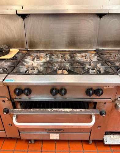 VULCAN COMMERCIAL SIX-BURNER NATURAL GAS RANGE WITH STANDARD OVEN BASE, HEAVY-DUTY CAST IRON OPEN-TOP GRATES, INDIVIDUAL BURNER CONTROLS, STAINLESS STEEL FRONT, BACKSPLASH, OVEN RACK, AND CASTERS.