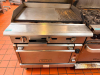 VULCAN COMMERCIAL NATURAL GAS GRIDDLE WITH STANDARD OVEN BASE, HEAVY-DUTY STEEL COOKING SURFACE WITH INTEGRATED RIBBED CHAR-GRILL SECTION, THREE FRONT BURNER CONTROLS, STAINLESS STEEL EXTERIOR, BACKSPLASH, AND CASTERS.
