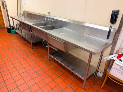 14' L X 28" D STAINLESS STEEL COMMERCIAL WORKTABLE AND TWO-COMPARTMENT SINK ASSEMBLY WITH INTEGRAL BACKSPLASH, LARGE WORK SURFACES, TWO DEEP SINK COMPARTMENTS, WALL-MOUNT FAUCET, TWO DRAWERS, LOWER STAINLESS STEEL STORAGE SHELVES, AND TUBULAR LEGS.