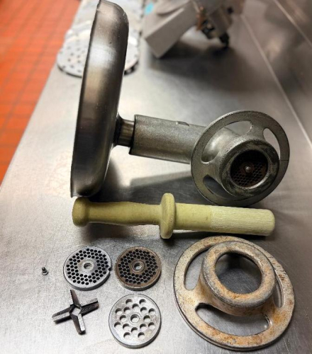 COMMERCIAL MEAT GRINDER ATTACHMENT ASSEMBLY WITH STAINLESS STEEL FEED PAN, GRINDER HEAD, WOODEN PRODUCT PUSHER, GRINDER KNIFE, MULTIPLE GRINDER PLATES, AND RETAINING RINGS.