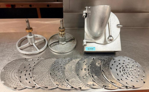 COMMERCIAL VEGETABLE SLICER / SHREDDER ATTACHMENT WITH CAST METAL HOUSING, HINGED FEED HOPPER, PUSHER ASSEMBLY, (2) DRIVE/PLATE HOLDERS, AND ASSORTED INTERCHANGEABLE SLICING, SHREDDING, AND GRATING DISCS.
