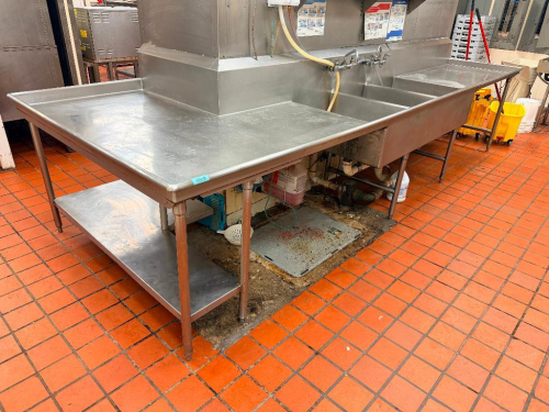 L SHAPED STAINLESS STEEL TWO-COMPARTMENT SINK WITH LARGE DRAINBOARD WORK SURFACES ON BOTH SIDES, INTEGRAL BACKSPLASH, DUAL DRAINS, WALL-MOUNT FAUCET ASSEMBLIES AND TUBULAR STAINLESS STEEL LEGS. LOWER STAINLESS STEEL UNDERSHELF PROVIDED BENEATH LEFT DRAIN