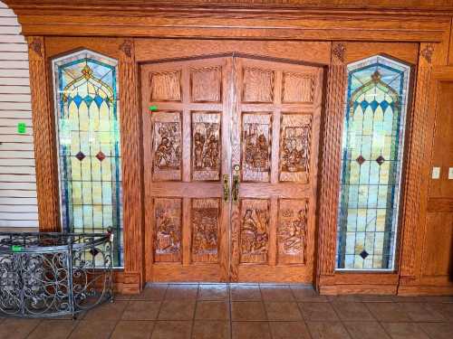 CUSTOM-BUILT SOLID OAK DOUBLE ENTRY DOOR ASSEMBLY WITH EXTENSIVE RELIEF-CARVED WINE AND VINEYARD SCENES, RAISED-PANEL CONSTRUCTION, DECORATIVE BRASS-TONE HARDWARE, HEAVY OAK CASING, AND MATCHING TALL LEADED STAINED-GLASS SIDELIGHTS. DECORATIVE GRAPE AND V