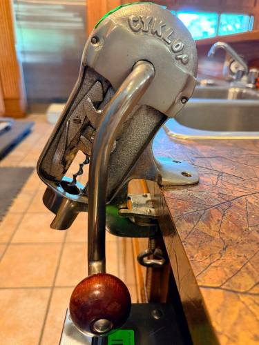 GYKLOP HEAVY-DUTY MANUAL BENCH-MOUNTED WINE BOTTLE CORKER WITH CAST METAL FRAME, LONG LEVER HANDLE, ADJUSTABLE BOTTLE PLATFORM, CORK COMPRESSION MECHANISM, AND COUNTER CLAMP.