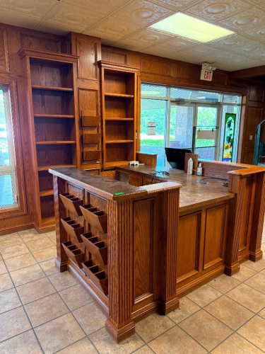 102" X 85" CUSTOM-BUILT U-SHAPED OAK RECEPTION / SERVICE COUNTER WITH RAISED TRANSACTION LEDGES, DECORATIVE FLUTED COLUMNS, RAISED-PANEL CABINETRY, DRAWERS, OPEN SHELVING, BUILT-IN LITERATURE / FILE SLOTS, AND DECORATIVE COUNTERTOP SURFACES. MATCHING FLOO
