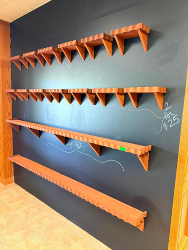 WOOD MERCHANDISER WALL SHELVING SYSTEM CONSISTING OF MULTIPLE WALL-MOUNTED SHELF SECTIONS WITH DECORATIVE SCALLOPED FRONT EDGES AND TRIANGULAR WOOD SUPPORT BRACKETS.