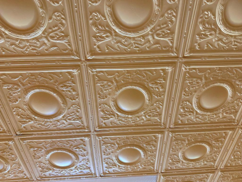 ALL DECORATIVE EMBOSSED PLASTIC CEILING TILE SYSTEM CONSISTING OF REPEATING SQUARE PANELS WITH ORNATE SCROLLWORK, FLORAL DETAIL, RAISED CENTER MEDALLIONS, AND MATCHING BORDER DETAIL. LOT INCLUDES ALL DECORATIVE PLASTIC CEILING TILES THROUGHOUT THE ROOM