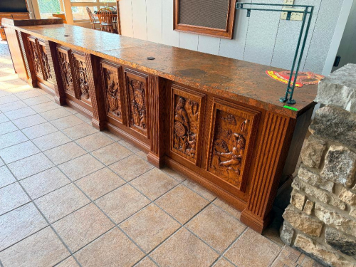 CUSTOM 14' WOOD BAR / SERVICE COUNTER WITH ORNATE CARVED RELIEF PANELS DEPICTING WINE, GRAPE HARVESTING, BARREL MAKING, CELLAR, AND VINEYARD SCENES. FLUTED WOOD COLUMNS SEPARATE THE CARVED PANELS. REAR SIDE INCLUDES OPEN STORAGE COMPARTMENTS, SHELVING, AN