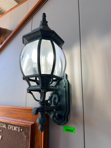 DECORATIVE WALL-MOUNT LANTERN LIGHT FIXTURE WITH BLACK FINISH, ORNATE BACKPLATE AND SUPPORT BRACKET, CLEAR CURVED GLASS PANELS, AND MULTI-LIGHT CANDELABRA-STYLE INTERIOR.