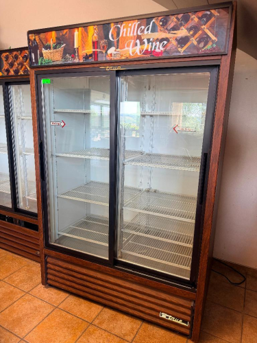 TRUE TWO-SECTION SLIDING GLASS DOOR REFRIGERATED MERCHANDISER WITH ADJUSTABLE INTERIOR WIRE SHELVING, BOTTOM-MOUNT REFRIGERATION SYSTEM, WOOD-GRAIN EXTERIOR FINISH, AND CHILLED WINE GRAPHIC HEADER.