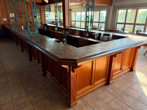30' X 10-1/2' U-SHAPED CUSTOM WOOD BAR WITH RAISED-PANEL OAK CABINETRY, DECORATIVE FLUTED COLUMNS AND CORBELS, DARK FINISHED COUNTERTOP, LOWER STORAGE CABINETS, DRAWERS, OPEN STORAGE SECTIONS, AND STAINLESS STEEL SINKS WITH FAUCETS.