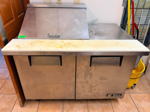 TRUE 48" TWO-DOOR REFRIGERATED SANDWICH / SALAD PREP TABLE WITH STAINLESS STEEL EXTERIOR, HINGED TOP PAN COMPARTMENT, FULL-WIDTH CUTTING BOARD, TWO LOWER REFRIGERATED SECTIONS, AND WIRE SHELVING.