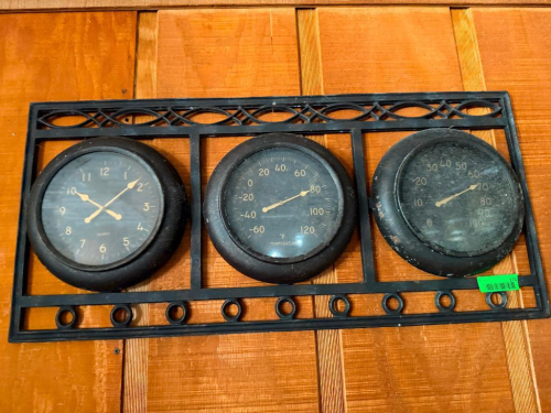 WALL-MOUNTED THREE-GAUGE DECORATIVE INSTRUMENT PANEL WITH CLOCK, FAHRENHEIT THERMOMETER, AND HUMIDITY GAUGE IN BLACK METAL FRAME.