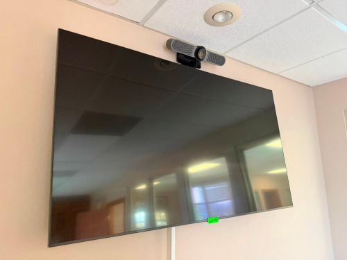 65" WALL-MOUNTED FLAT SCREEN TELEVISION WITH EXTERNAL VIDEO CONFERENCING CAMERA / SOUNDBAR MOUNTED ABOVE DISPLAY.