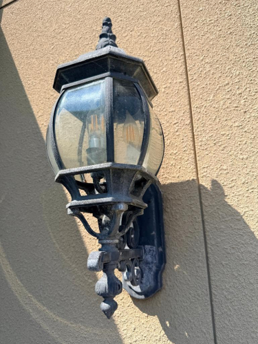 (6) DECORATIVE WALL-MOUNT LANTERN LIGHT FIXTURE WITH BLACK FINISH, ORNATE BACKPLATE AND SUPPORT BRACKET, CLEAR CURVED GLASS PANELS, AND MULTI-LIGHT CANDELABRA-STYLE INTERIOR.