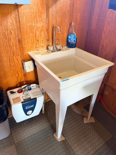 FREESTANDING UTILITY SINK WITH DEEP MOLDED BASIN, FOUR-LEG SUPPORT, DUAL-HANDLE FAUCET AND UNDER-SINK ELECTRIC WATER HEATER.