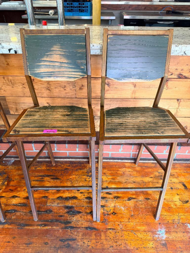 (2) WOOD AND METAL BAR HEIGHT CHAIRS WITH SOLID WOOD SEATS AND BACKREST PANELS, SQUARE TUBULAR STEEL FRAMES, AND INTEGRATED FOOTRESTS. DISTRESSED DARK FINISH