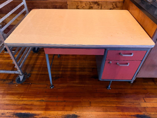 48" WIDE X 30" VINTAGE METAL OFFICE DESK WITH LAMINATE WORK SURFACE, STEEL FRAME, SINGLE PEDESTAL STORAGE SECTION, BOX DRAWER, LOWER FILE DRAWER, CENTER PENCIL DRAWER, METAL PULL HANDLES, LOCK, AND ADJUSTABLE FEET. BEIGE LAMINATE TOP WITH PINK/RED AND GRA
