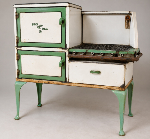 QUICK MEAL VINTAGE PORCELAIN ENAMEL GAS RANGE WITH WHITE AND GREEN FINISH, CAST-IRON COOKING GRATES, EXPOSED FRONT GAS MANIFOLD, MULTIPLE BURNER CONTROL POSITIONS, DOUBLE OVEN/WARMING COMPARTMENTS, LOWER STORAGE DRAWER, AND CAST METAL LEGS.