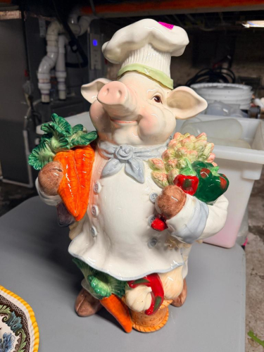 DECORATIVE CERAMIC CHEF PIG FIGURINE FEATURING A PIG DRESSED IN A CHEF COAT AND HAT HOLDING ASSORTED VEGETABLES INCLUDING CARROTS, ARTICHOKE, PEPPERS, ONION, AND OTHER PRODUCE. GLAZED MULTICOLOR CERAMIC CONSTRUCTION WITH THREE-DIMENSIONAL MOLDED DETAILS.