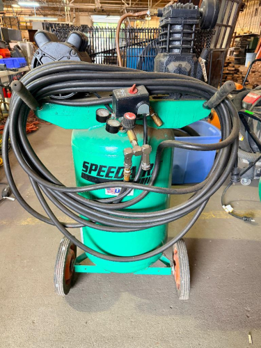 SPEEDAIRE PORTABLE VERTICAL ELECTRIC AIR COMPRESSOR WITH 20-GALLON AIR RECEIVER, OIL-LUBRICATED PUMP, PRESSURE REGULATOR, DUAL PRESSURE GAUGES, WHEELS, HANDLE, AND AIR HOSES.