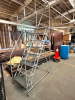 ROLLING INDUSTRIAL STEEL ACCESS LADDER WITH MULTIPLE TREAD STEPS, UPPER WORK PLATFORM, FULL-LENGTH HANDRAILS, SAFETY RAIL FRAME, AND CASTER BASE.