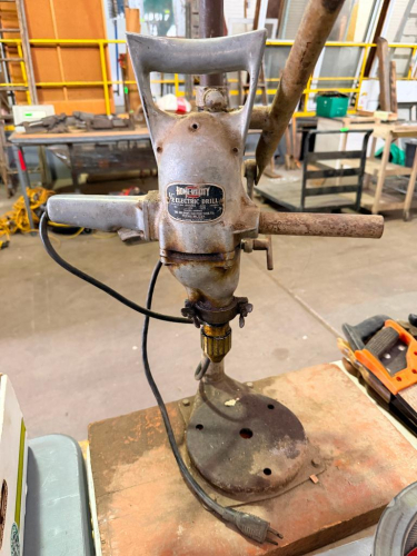 VINTAGE HEAVY-DUTY 1/2" ELECTRIC DRILL MOUNTED ON A BENCH-TOP DRILL PRESS STAND WITH KEYED CHUCK, DUAL SIDE HANDLES, MANUAL FEED LEVER, VERTICAL COLUMN, AND CAST METAL BASE.
