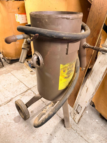 PRESSURIZED ABRASIVE BLAST POT WITH STEEL PRESSURE VESSEL, WHEELED FRAME, BLAST HOSE, CONTROL VALVES, AIR CONNECTIONS AND ABRASIVE FILL OPENING.